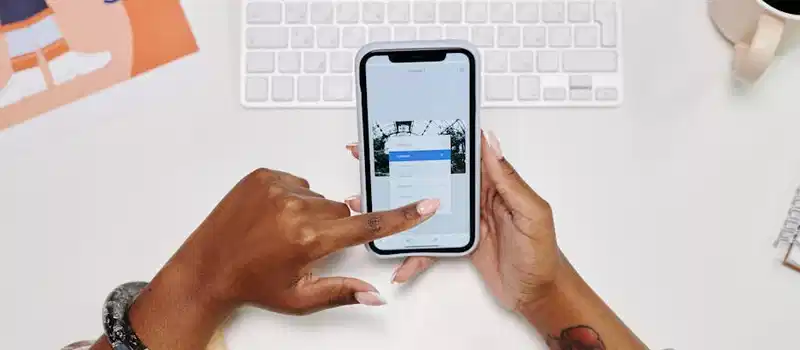 Close-up of hands using a smartphone at a desk with a keyboard and coffee cup.
