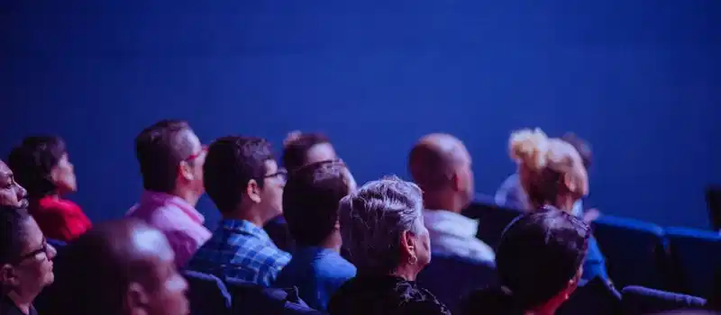 An attentive group of adults seated at an indoor conference, focusing on a presentation.