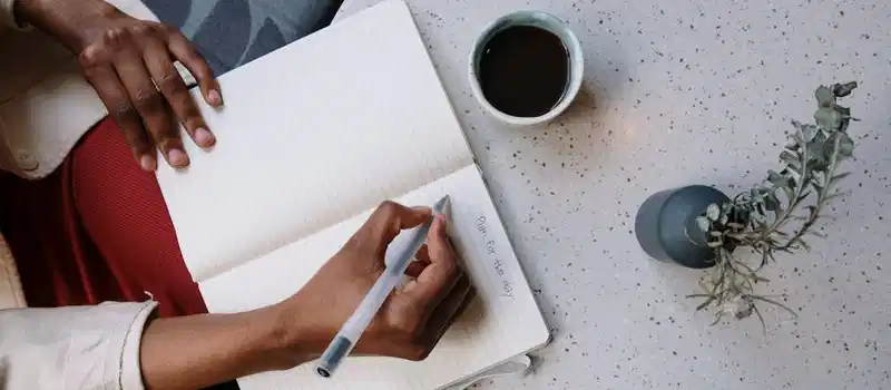 Person writing in a planner with coffee at a café, focusing on planning and productivity.