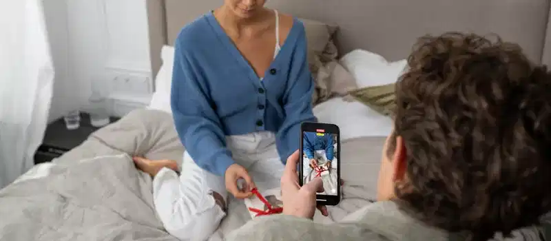Couple filming unboxing video in a cozy bedroom setting with a smartphone.