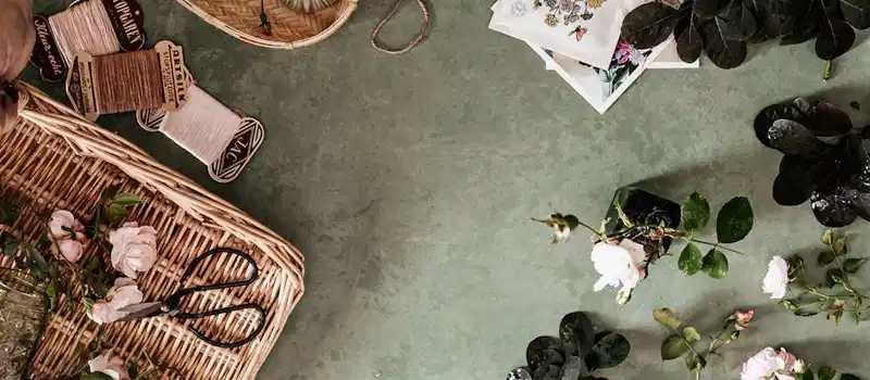 Flat lay of floral arrangement with baskets, roses, and vintage twine on a green surface.