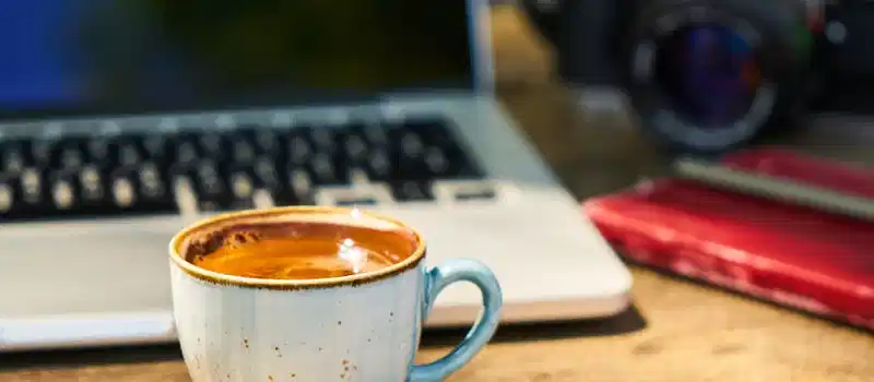 A cozy workspace with a cappuccino, laptop, and vintage camera on a wooden desk.