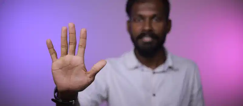 Close-up of a man extending his hand towards the camera against a colorful background.