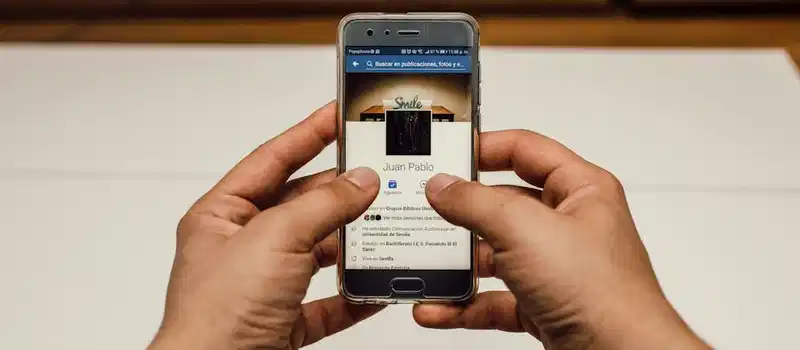 Close-up of hands using a smartphone with a social media page indoors.