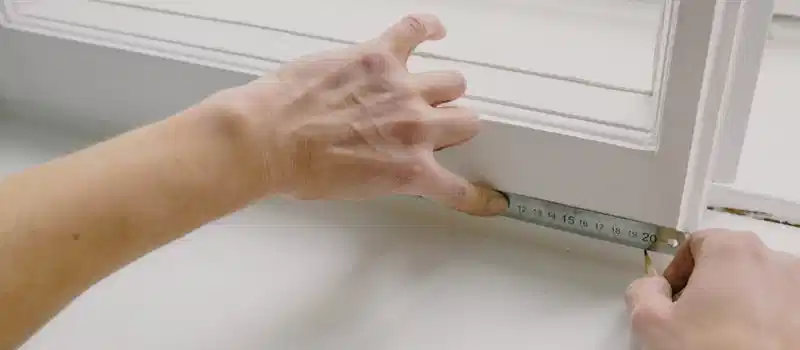 From above of crop anonymous workman measuring wooden window frame using metal ruler and pencil in house