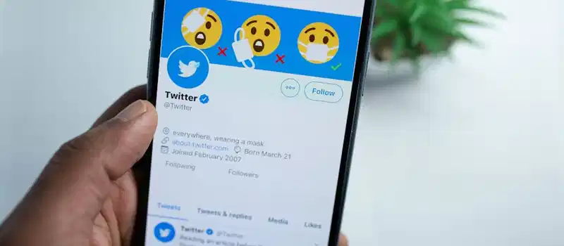 A close-up of a hand holding a smartphone showing a Twitter profile, emphasizing social media engagement.
