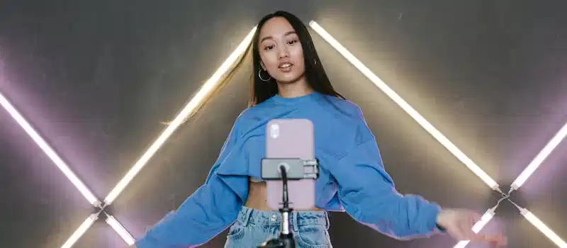 Teen influencer dances stylishly indoors, creating content using smartphone and ring light.