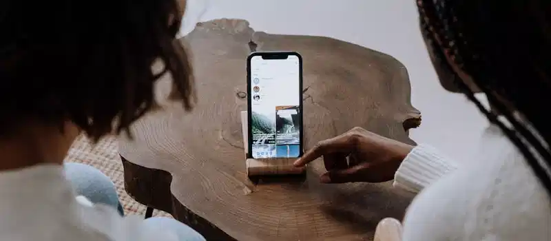 Adults explore social media on a smartphone resting on a unique wooden table.