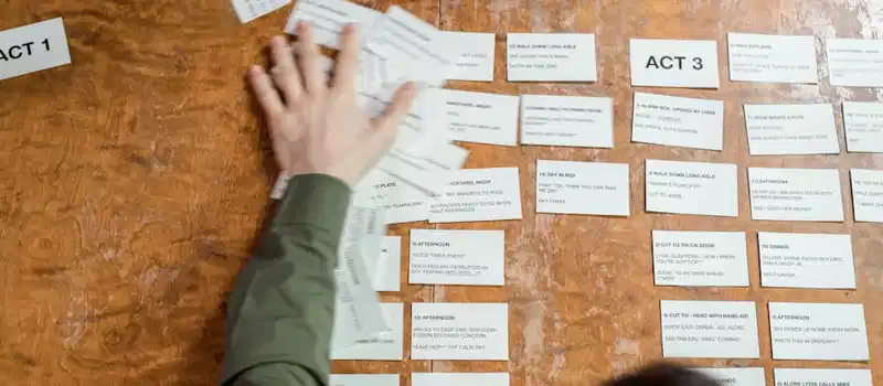 A person arranging storyboard cards on a wooden table for a film script planning session.