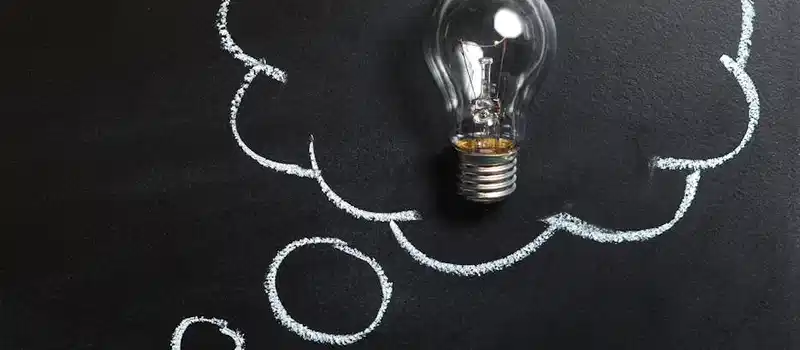 Light bulb laying on chalkboard with drawn thought bubble, symbolizing creative ideas.