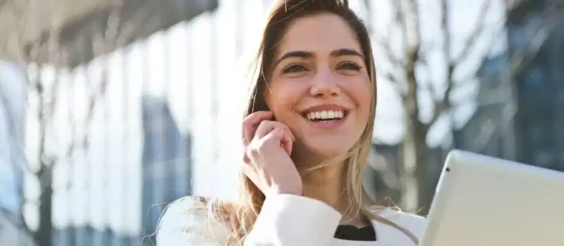 Confident businesswoman using her tablet and phone, smiling outdoors in sunlight.