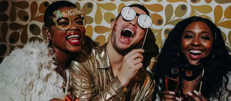 Three friends in festive outfits celebrate New Year's Eve with props and laughter.