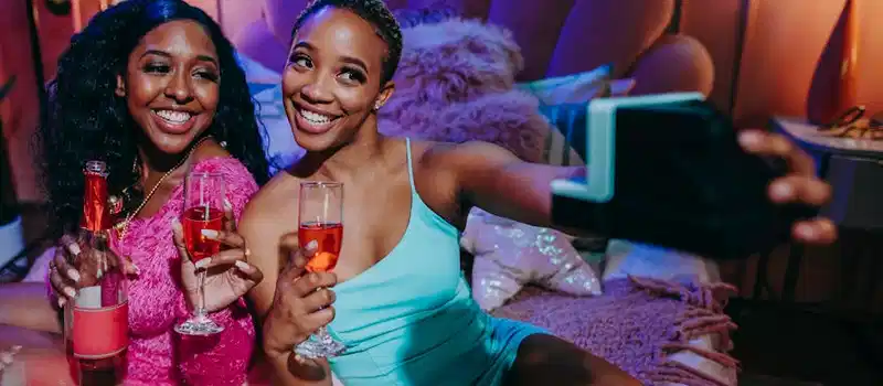 Two young women enjoying a festive indoor celebration with drinks and a friendly atmosphere.