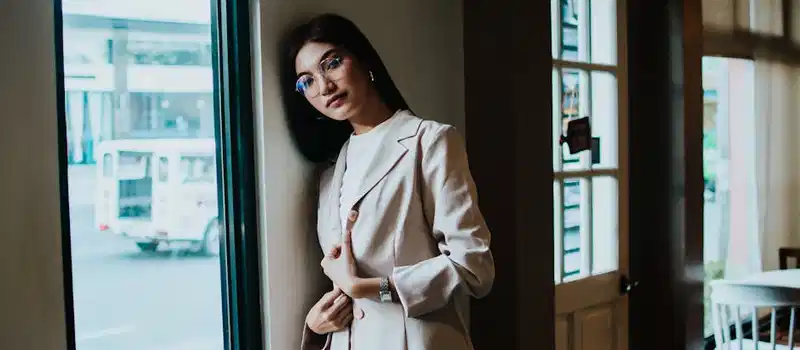 A fashionable woman in a chic outfit posing indoors by a window, capturing natural light.