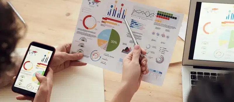 Team members analyze charts during a business meeting with laptops and smartphones.