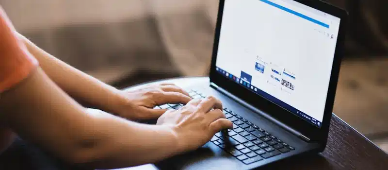 Close-up of person typing on a laptop indoors, showcasing technology use.