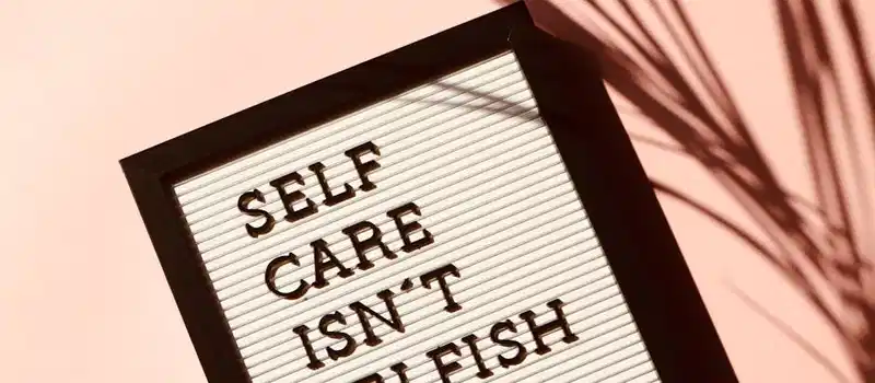 Letter board displaying 'Self Care Isn't Selfish' with artistic shadow on pink background.
