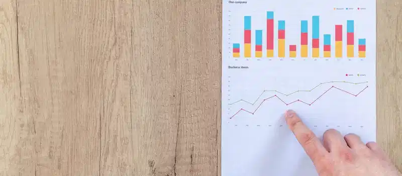 Hand analyzing business graphs on a wooden desk, focusing on data results and growth analysis.