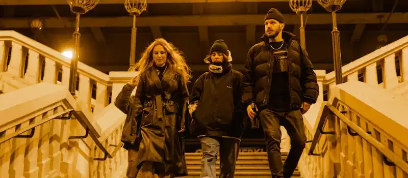 Three friends walk down stairs at night, under warm streetlights.