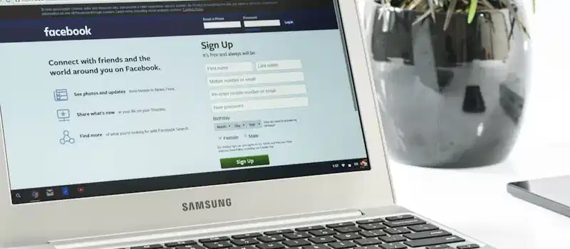 Open Samsung laptop showing Facebook sign-up page next to a potted plant. Ideal for technology themes.