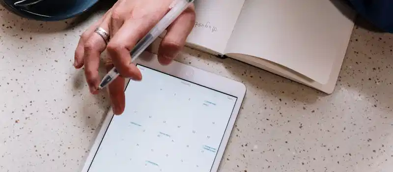 Person using a tablet for planning with an open notebook and coffee. Ideal for tech and productivity visuals.