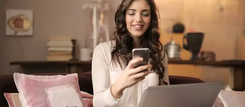 A woman enjoying leisure time using her smartphone and laptop in a cozy living room.