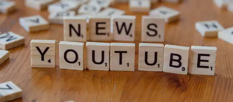 Scrabble tiles spelling words on wooden surface, focusing on YouTube and News.