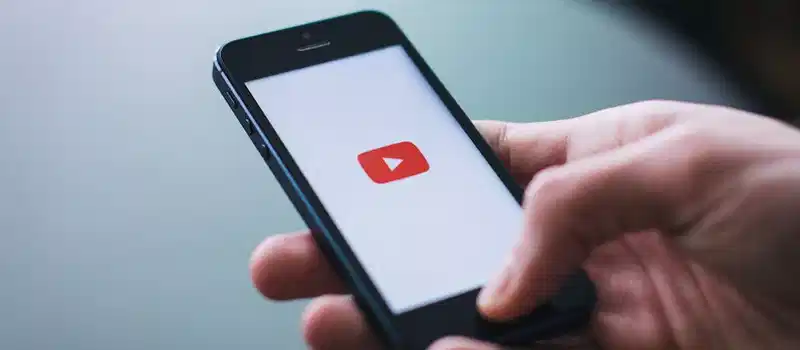 Close-up of a hand holding a smartphone displaying the YouTube app on the screen.