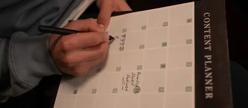Close-up of hands writing in a content planner for organizational purposes.