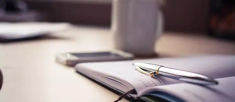 Cozy workspace with an open planner, pen, and coffee mug on a desk.