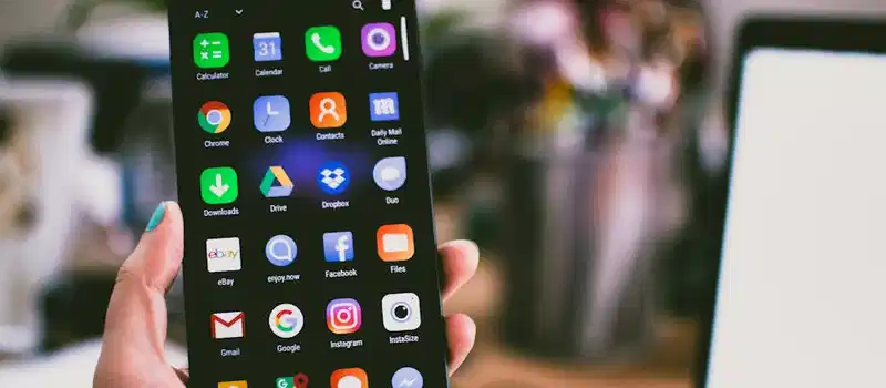 A close-up image of a person's hand holding a smartphone displaying various popular apps.