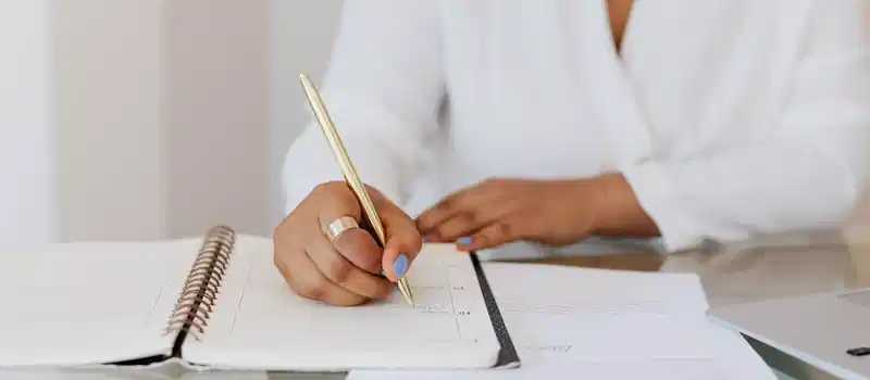 Close-up of a person writing notes in a planner with a gold pen, emphasizing organization.