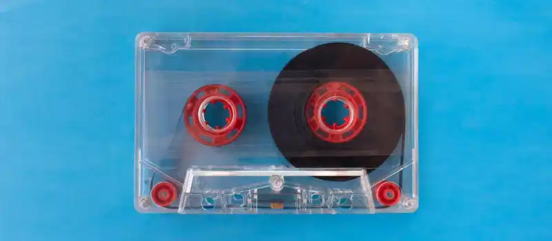 Vintage transparent cassette tape with red reels on a bright blue background.