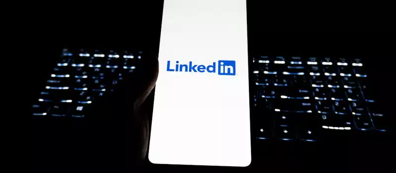 Close-up of LinkedIn logo on smartphone with backlit keyboard in dark room.