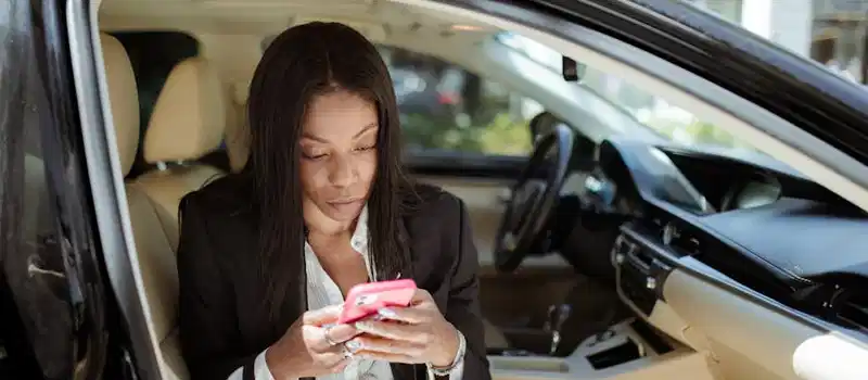 A businesswoman uses her smartphone while seated in a car, focusing intently on the screen.