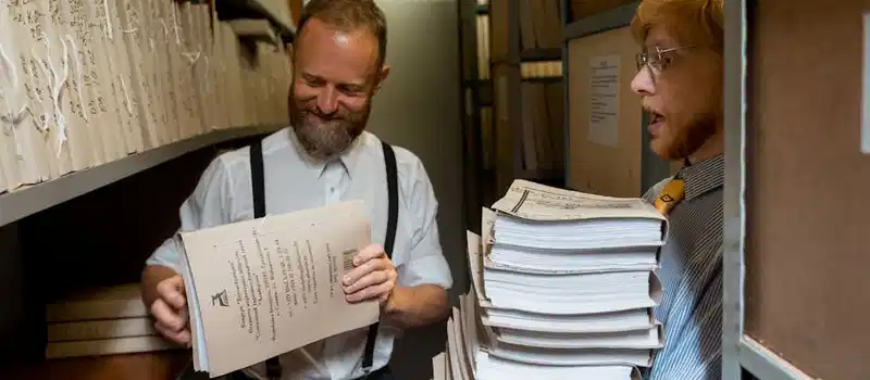 Two men sorting through stacks of documents in an archive room, showcasing teamwork and organization.