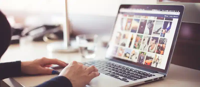 Close-up of hands typing on a laptop with an image gallery open on the screen.