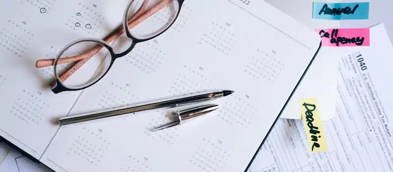 Overhead view of a desk with glasses, a pen, calendar, and tax documents.