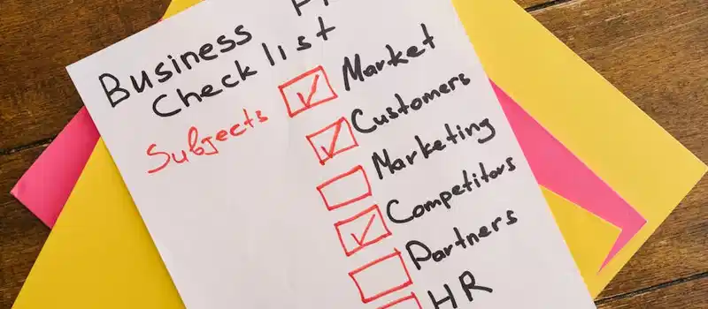 A handwritten business plan checklist on a table with colorful papers indicating important topics for startups.