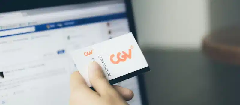 Close-up of a hand holding a card near an active laptop screen, indoors.