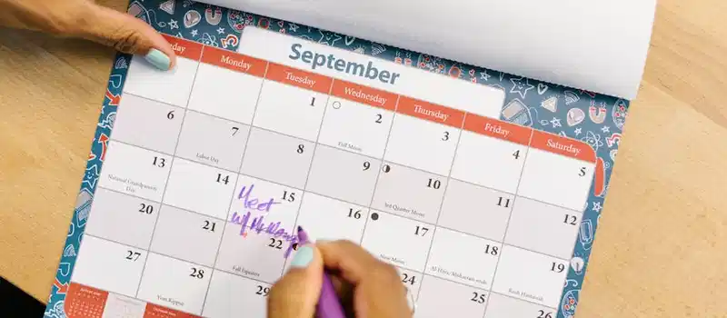 A person marking a calendar in September with a purple pen on a wooden desk.