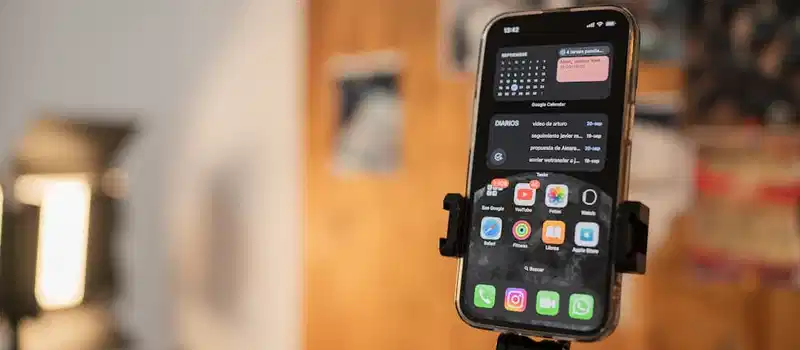 Close-up of a smartphone held on a tripod indoors with apps displayed on screen.