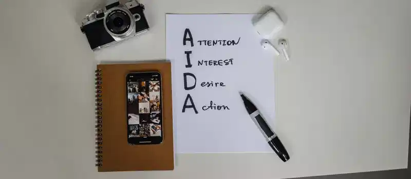 Top view of AIDA marketing elements with notebook, smartphone, camera, and earbuds on a desk.